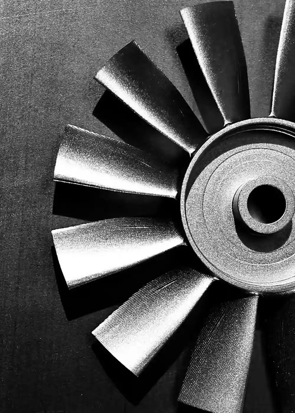 Black-and-white close-up of a multi-blade brushless fan rotor positioned on the right, set against a dark, vertically-textured metal backdrop.