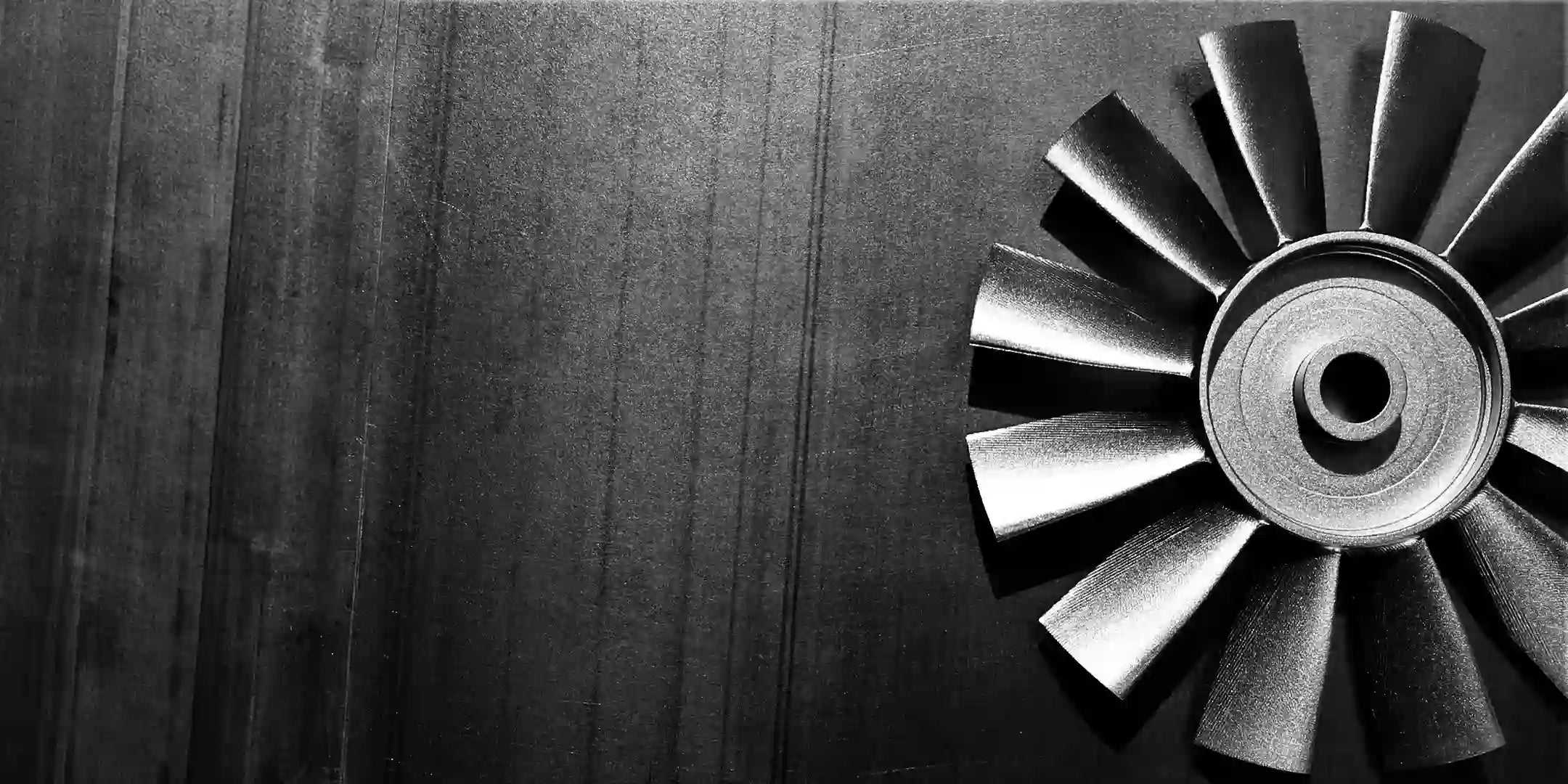 Black-and-white close-up of a multi-blade brushless fan rotor positioned on the right, set against a dark, vertically-textured metal backdrop.