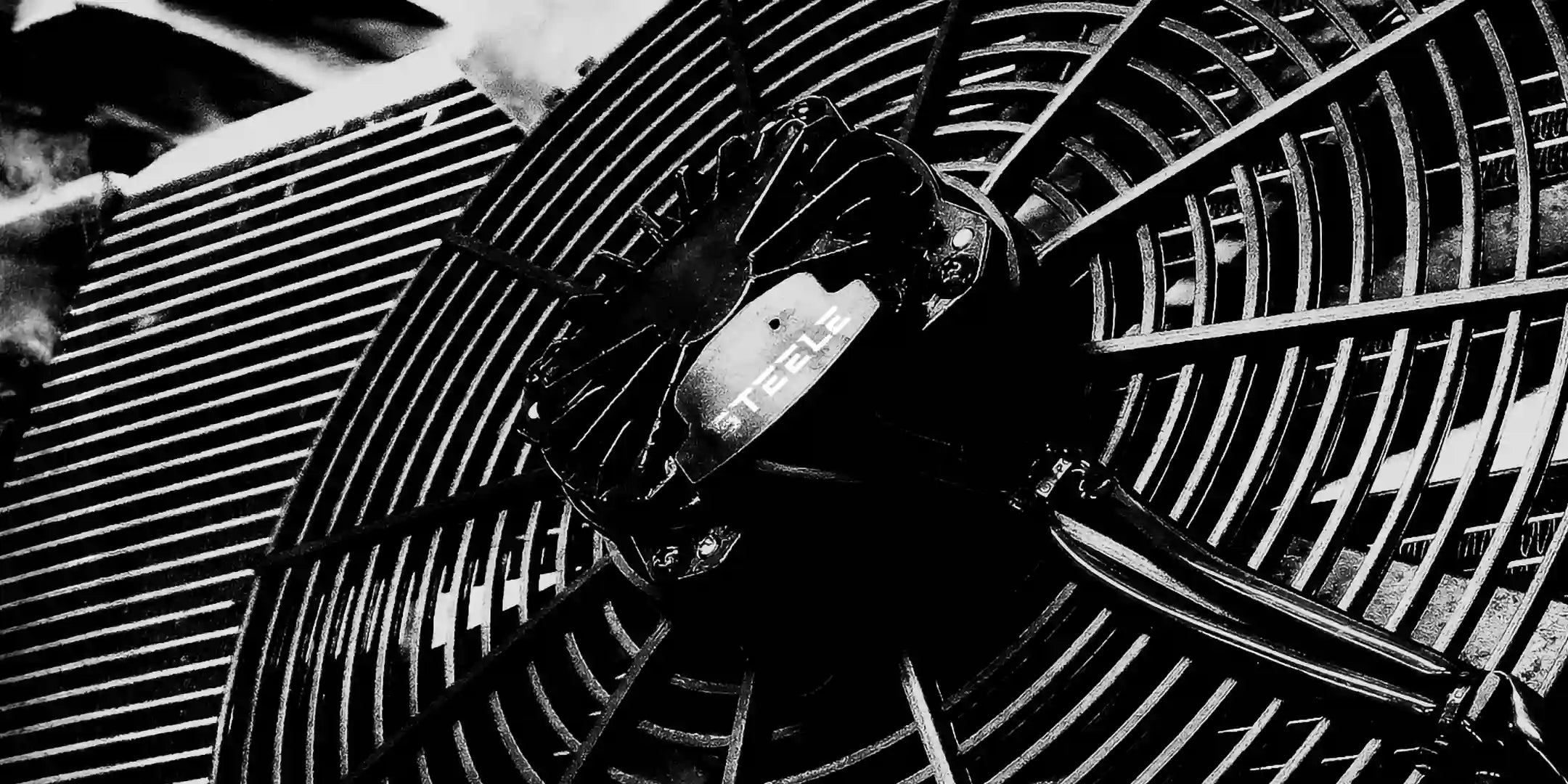 Close-up of a STEELE high-performance brushless radiator fan, showing detailed motor housing and curved fan blades with a high-contrast, industrial black and white aesthetic.